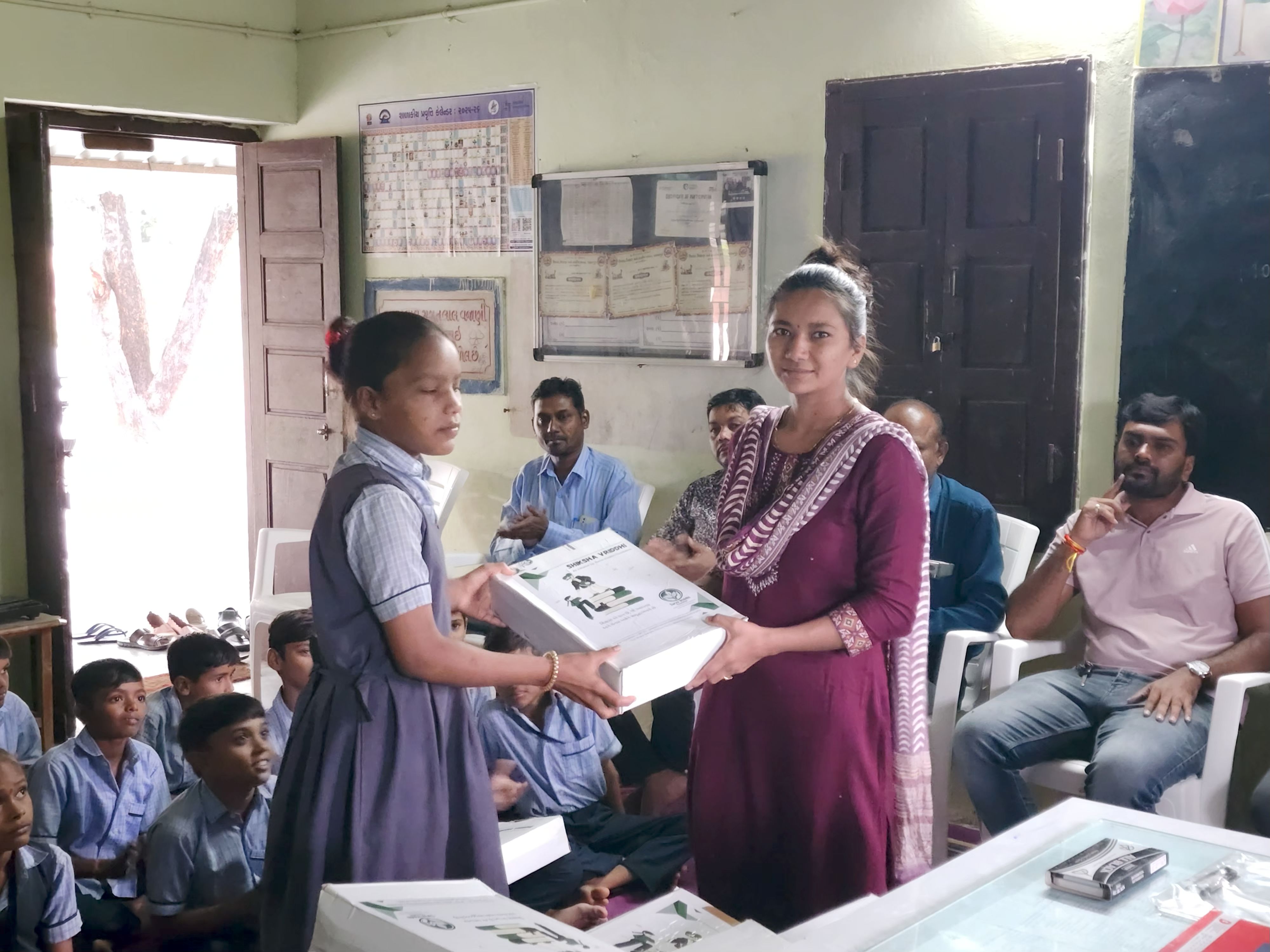 Girl receiving educational kit from a woman in maroon shawl